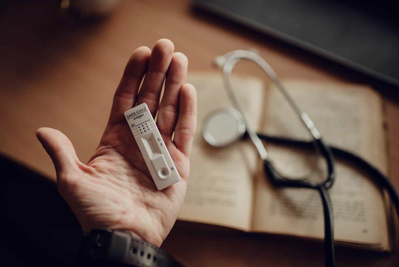 Hand holding a small test device beside a stethoscope and an open book