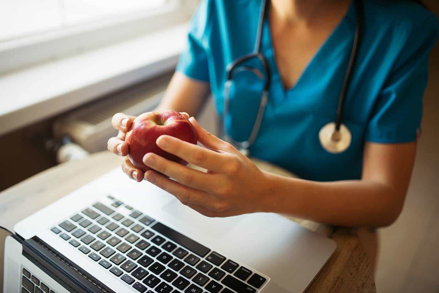 Nurse holding an apple next to a laptop